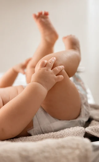 Ein Baby greift beim Liegen nach seinem Bein, mit kleinen Händen und Füßen im Fokus