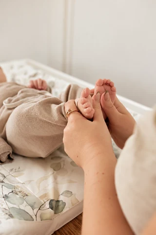 Hände halten behutsam die Füße eines Babys auf einer weichen Unterlage