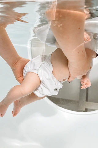 Hände begleiten ein Baby beim Floating im Wasser