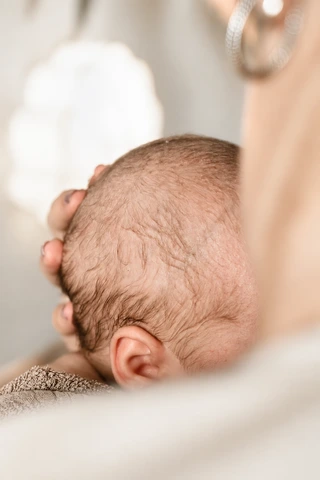 Eine Hand hält behutsam den Kopf eines angekuschelten Babys
