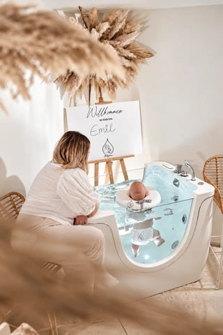 Eine Bezugsperson sitzt neben ihrem Baby an der Floating-Wanne